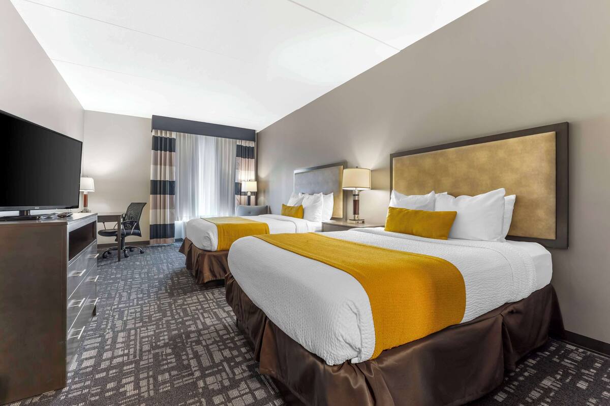 A hotel room with two beds, a desk, a television, and a large window with curtains.