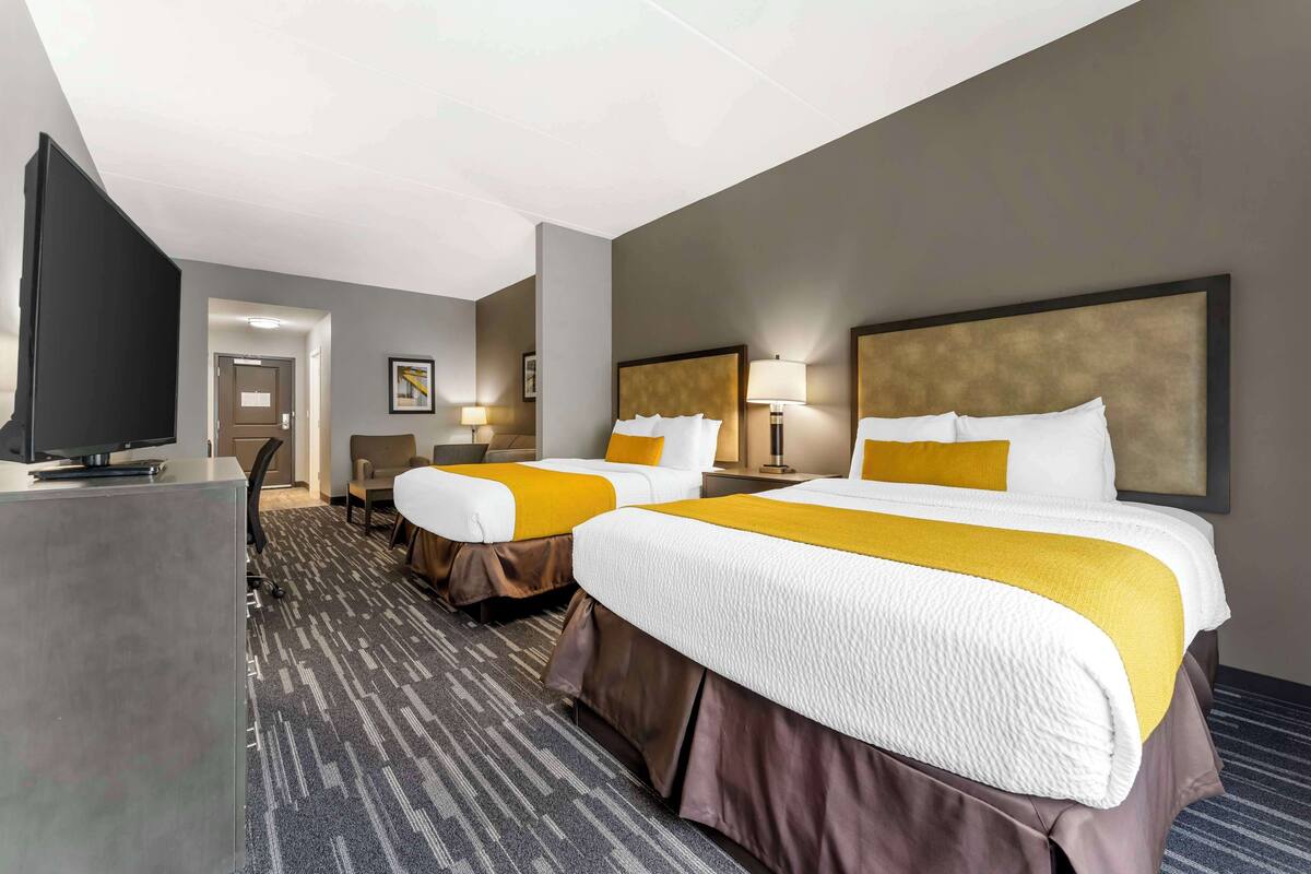 A hotel room with two beds, a desk, and a television.
