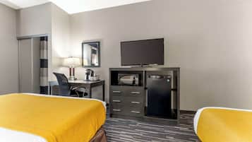 A hotel room with two beds, a desk with a computer, a flat-screen TV, a microwave, and a refrigerator.