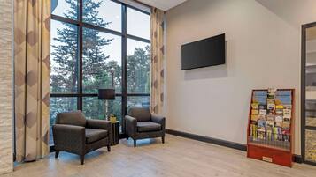 A room with two armchairs, a flat-screen TV, a bulletin board, and a large window with a view of trees.