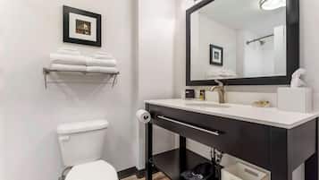 A modern bathroom with a white toilet, a black vanity with a mirror, and a shelf with folded towels.