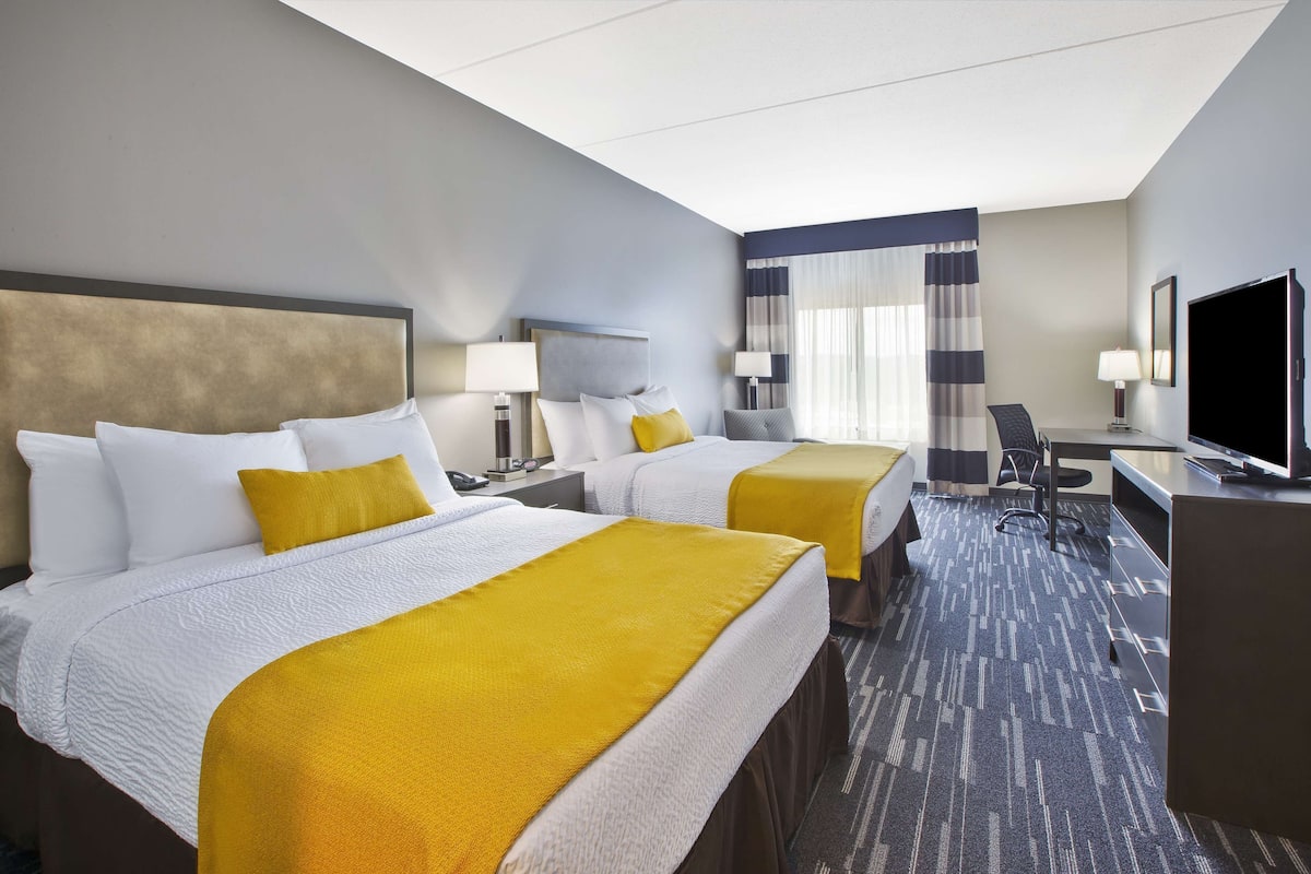 A hotel room with two beds, a desk, a TV, and a window with curtains.