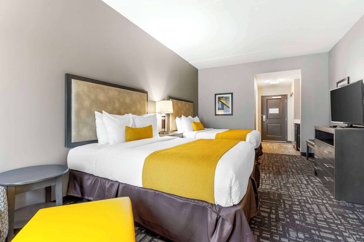 A hotel room with a large bed, a desk, a chair, a TV, and a door leading to a hallway.