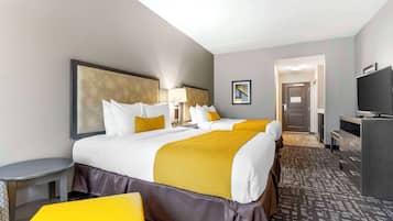 Een hotelkamer met een groot bed, een bureau, een stoel, een televisie en een deur naar een gang.