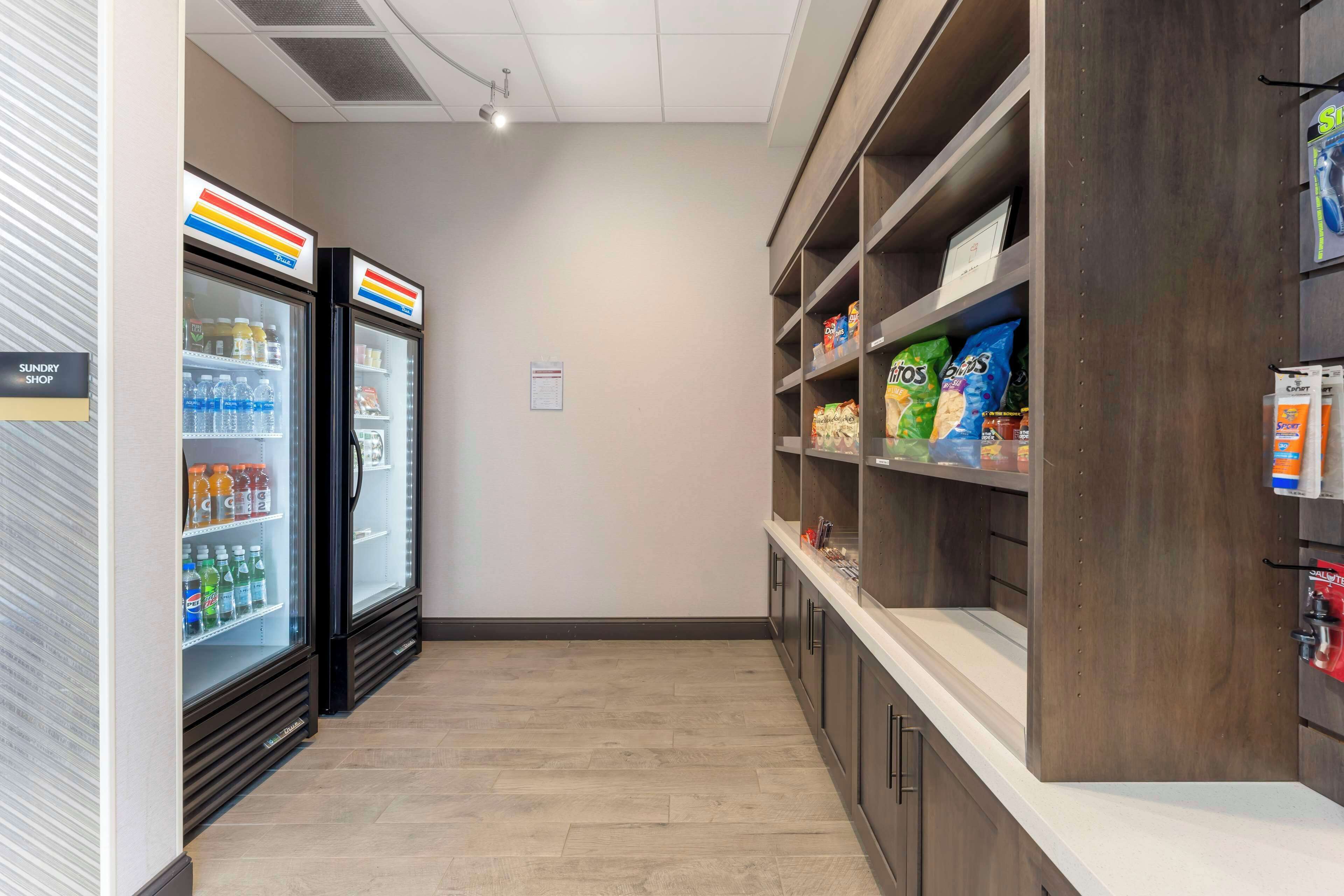 A narrow hallway with a refrigerated display case on the left and shelves stocked with snacks on the right.