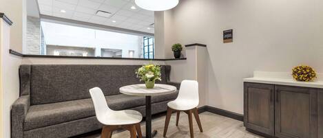 A modern lounge area with a grey sofa, two white chairs, a round table, and a coffee bar.