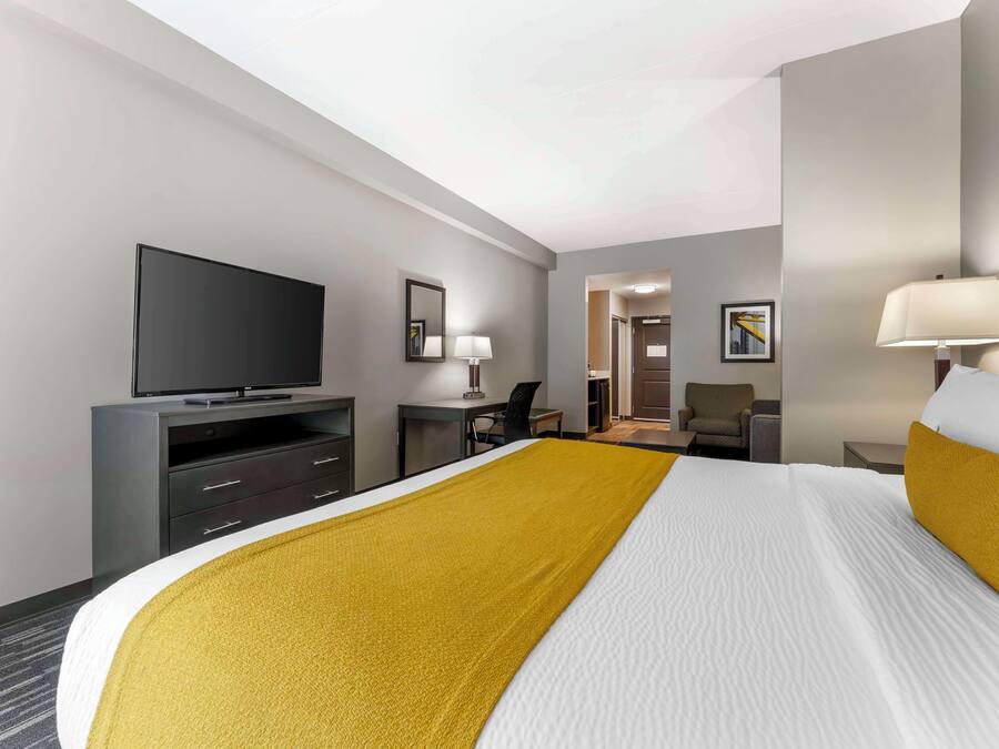 A hotel room with a large bed, a flat-screen TV, a desk with a chair, a lamp, and a framed picture on the wall.