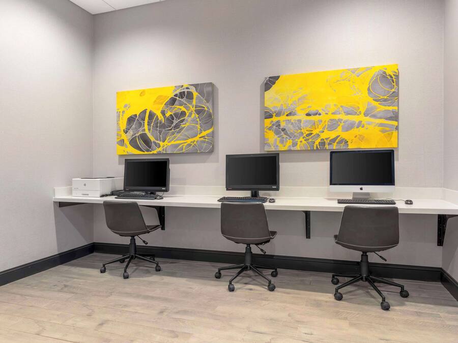 A modern office space with three desks, each with a computer monitor and keyboard, and two office chairs.