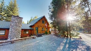 A log cabin with a stone chimney, a flag, and a gravel driveway. - 33 MI to YNP | Private Dock | Firepit (Island Park)
