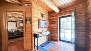 A cabin interior with a wooden floor, a desk with drawers, a framed picture on the wall, and a door leading outside. - 33 MI to YNP | Private Dock | Firepit (Island Park)