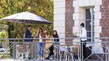 Un groupe de personnes est assis à la terrasse d’un café, avec une rambarde en métal et des chaises en osier.