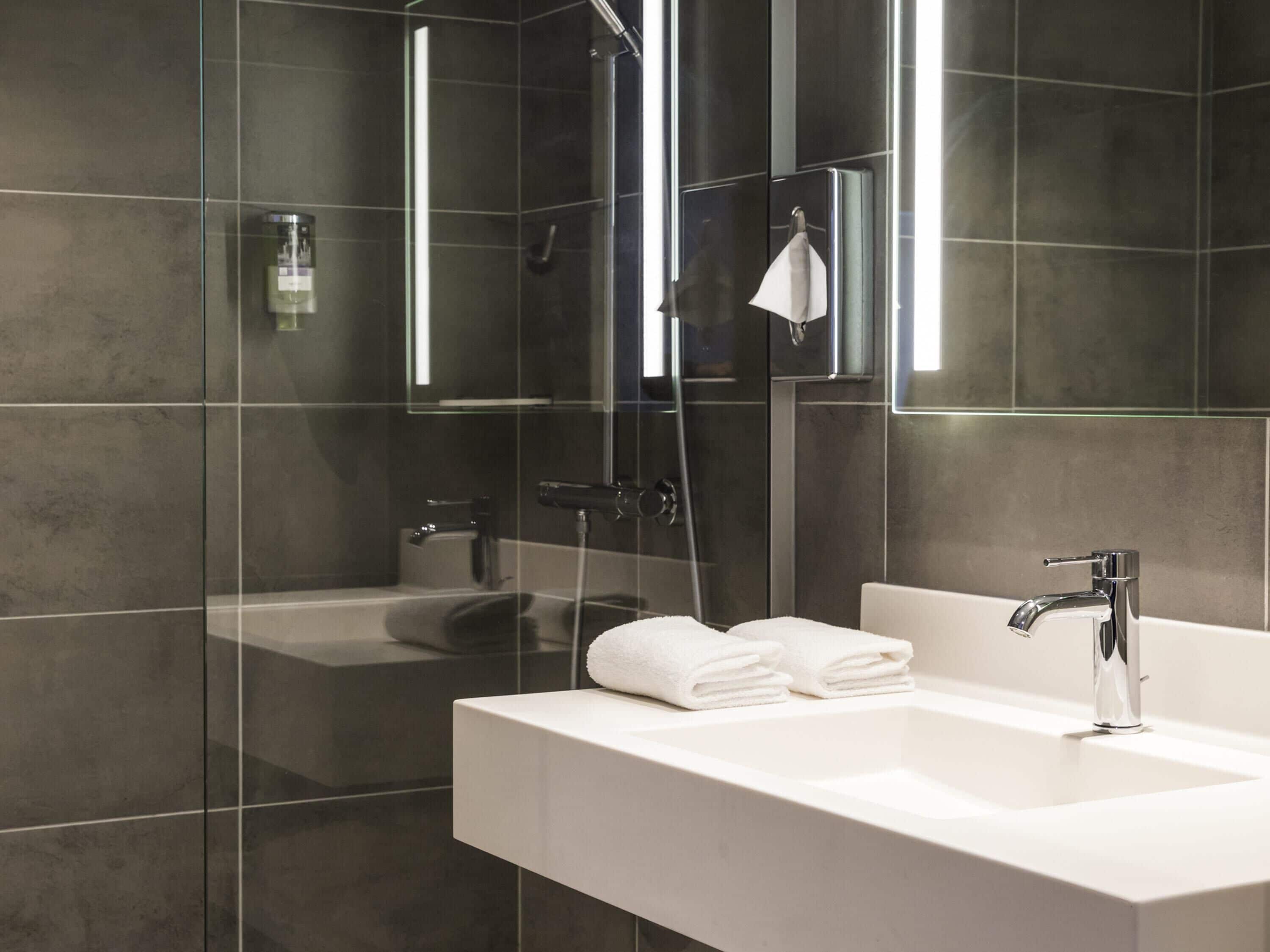 A modern bathroom with a glass-enclosed shower, a white sink, and a mirror.