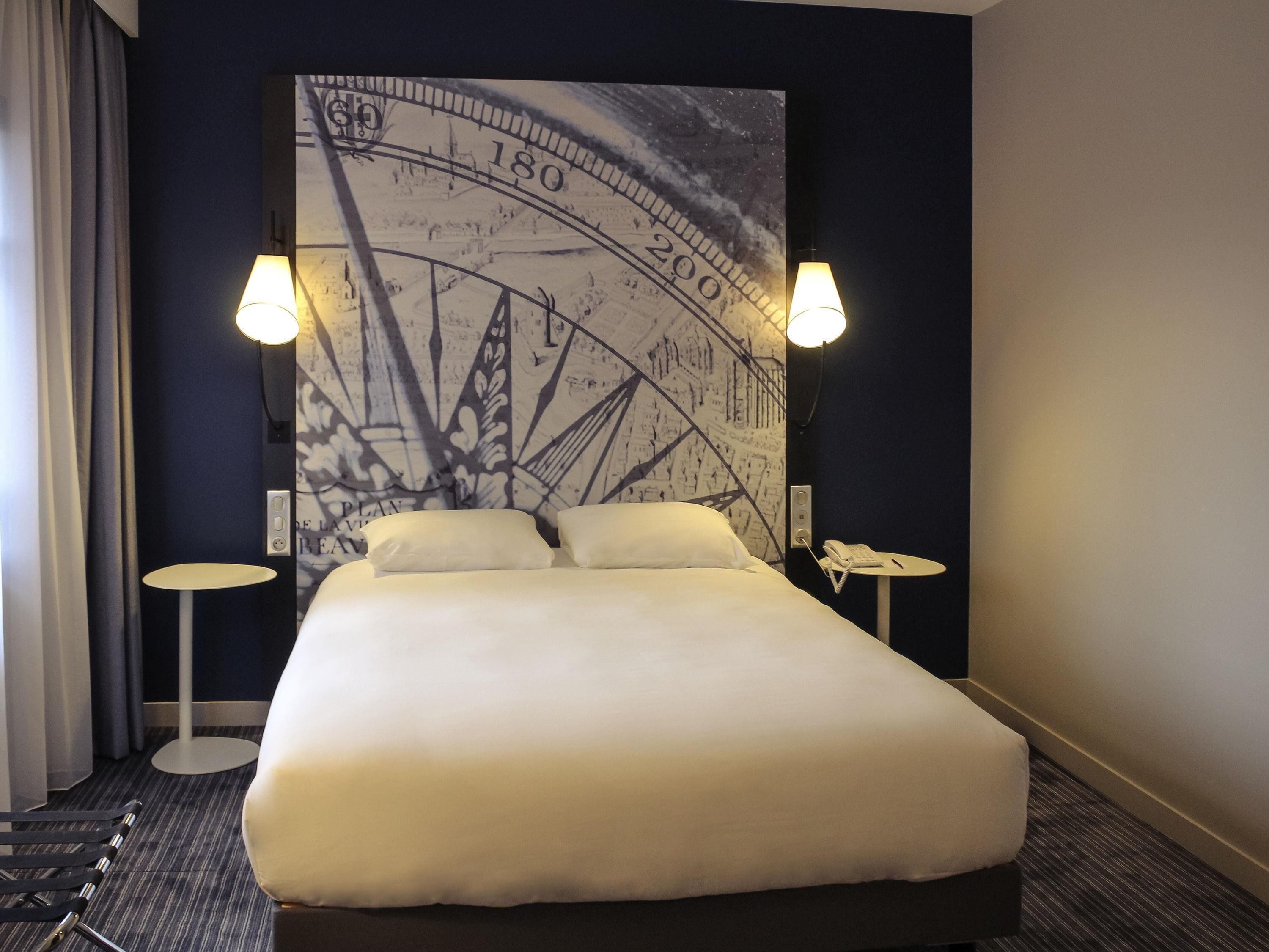 Une chambre d’hôtel avec un lit, deux lampes de chevet, une horloge murale et un téléphone posé sur une petite table.