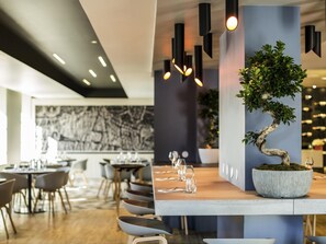 A modern restaurant interior with a long dining table, chairs, and a bonsai tree centerpiece. - Hôtel Mercure Beauvais Centre Cathédrale (Beauvais)