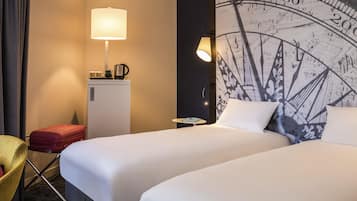 Habitación de hotel con dos camas, un escritorio, una lámpara, un refrigerador pequeño y una silla.