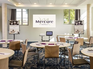 Sala de conferência com mesas redondas, cadeiras, uma tela de projetor e banners para Mercure Hotels.
