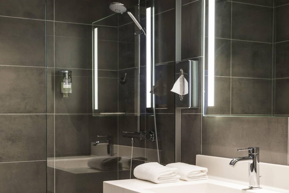A modern bathroom with a glass-enclosed shower, a white sink, and a large mirror.