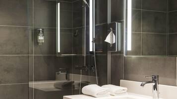 Un baño moderno con ducha de vidrio, lavamanos blanco y un espejo grande.