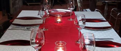 A restaurant with a long table set for a meal, featuring red tablecloths and wine glasses.