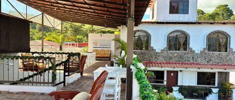 A hotel with a covered outdoor area featuring wooden furniture and a staircase leading to a second floor.