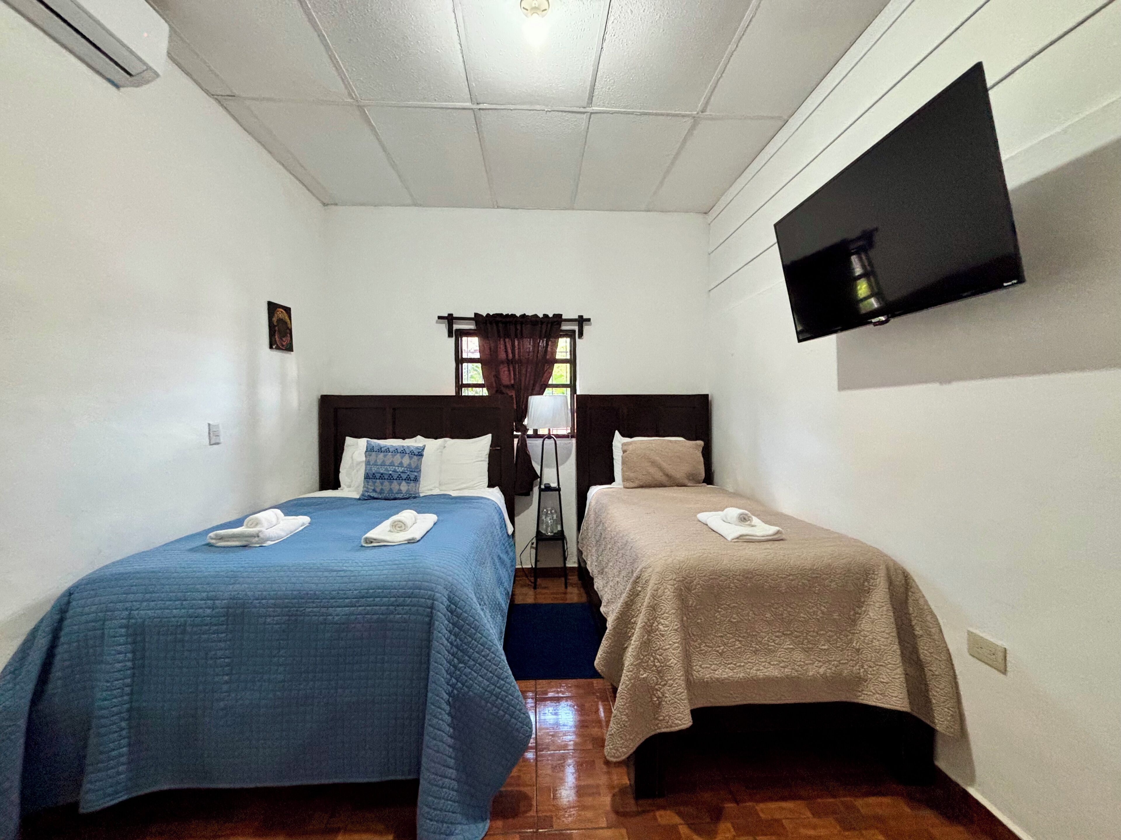 A hotel room with two beds, each with a different colored bedspread, a TV mounted on the wall, and a window with curtains.