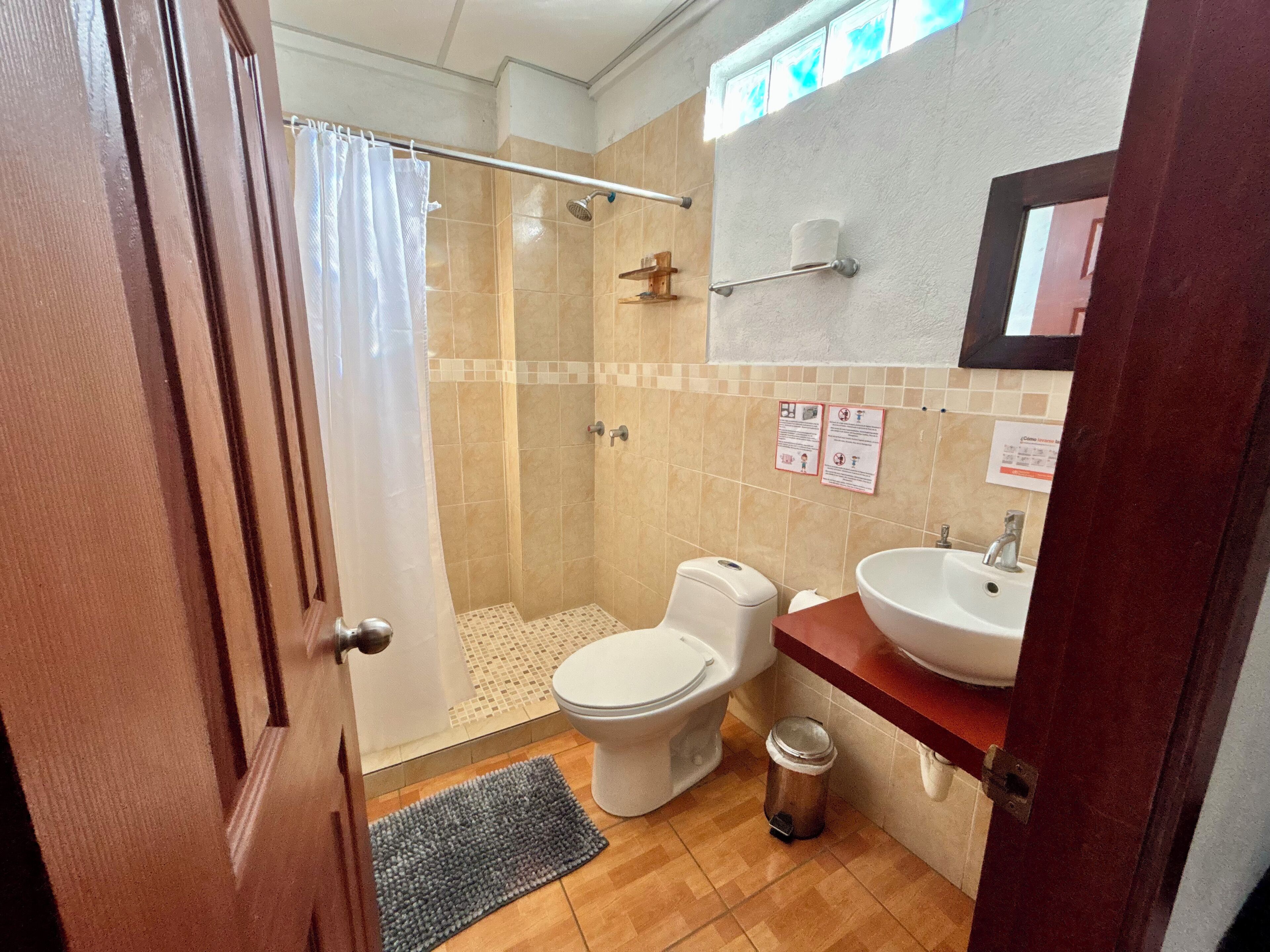 A bathroom with a shower, toilet, sink, and a trash bin.