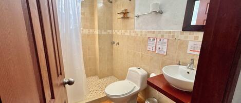 A bathroom with a shower, toilet, sink, and a trash bin.