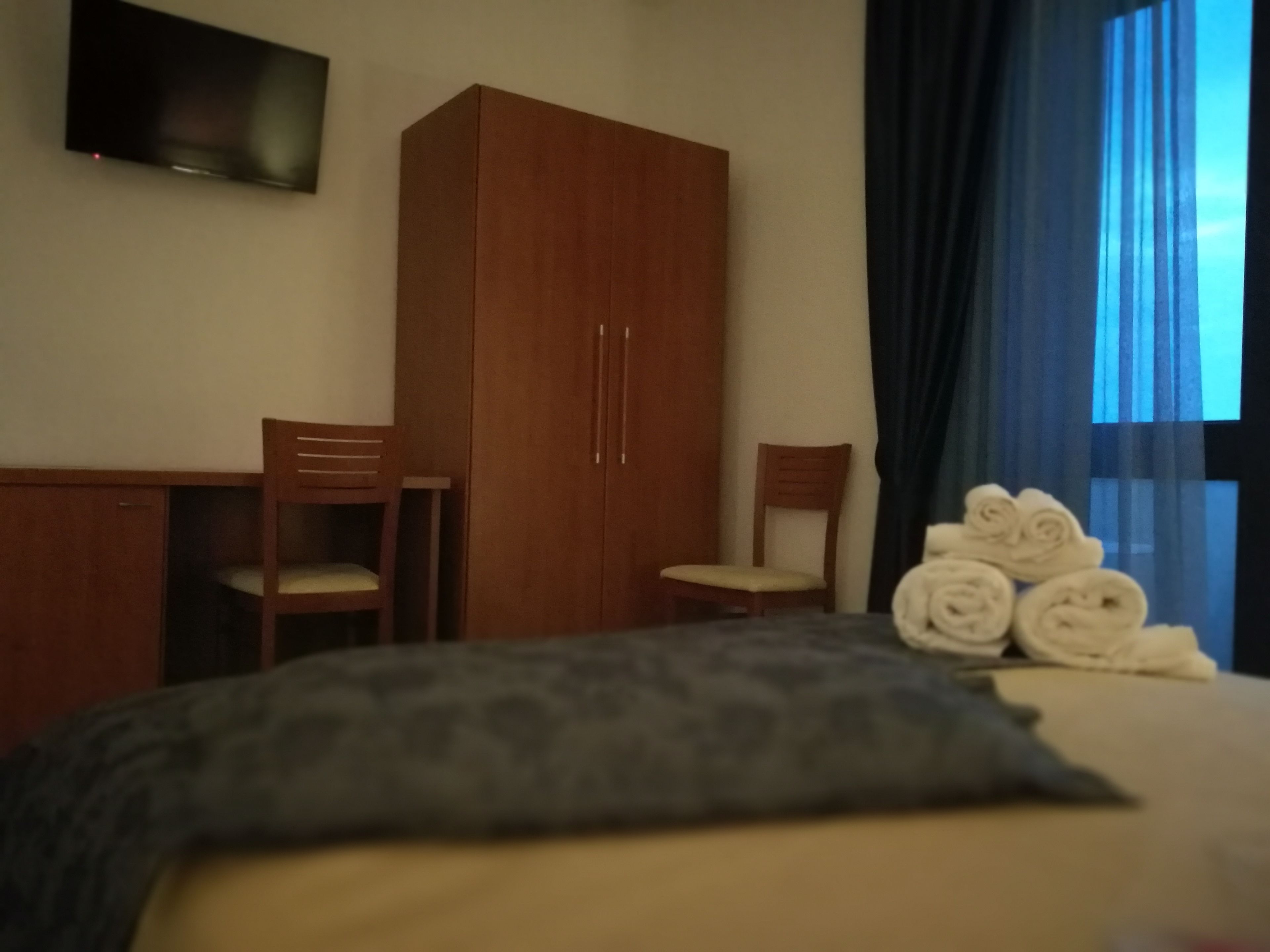 Ein Hotelzimmer mit Bett, Holzschrank, Schreibtisch, zwei Stühlen und einem an der Wand befestigten Fernseher.