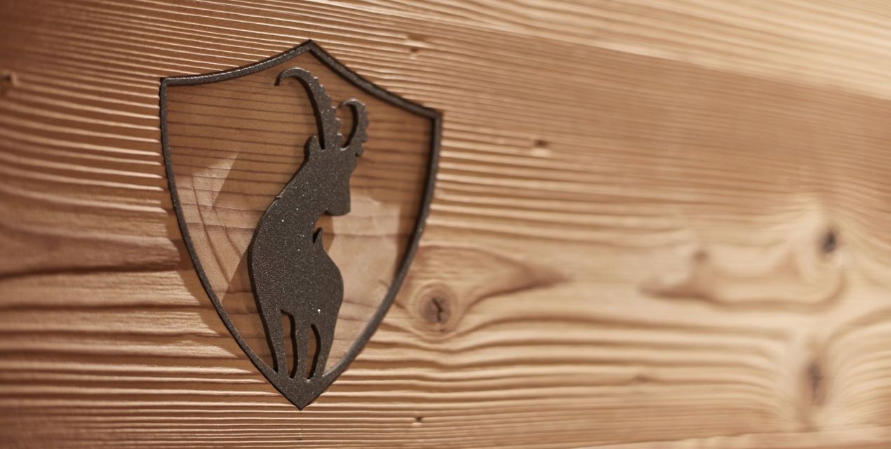 Un emblema con forma de escudo que muestra el silueta de un ciervo sobre una superficie de madera.
