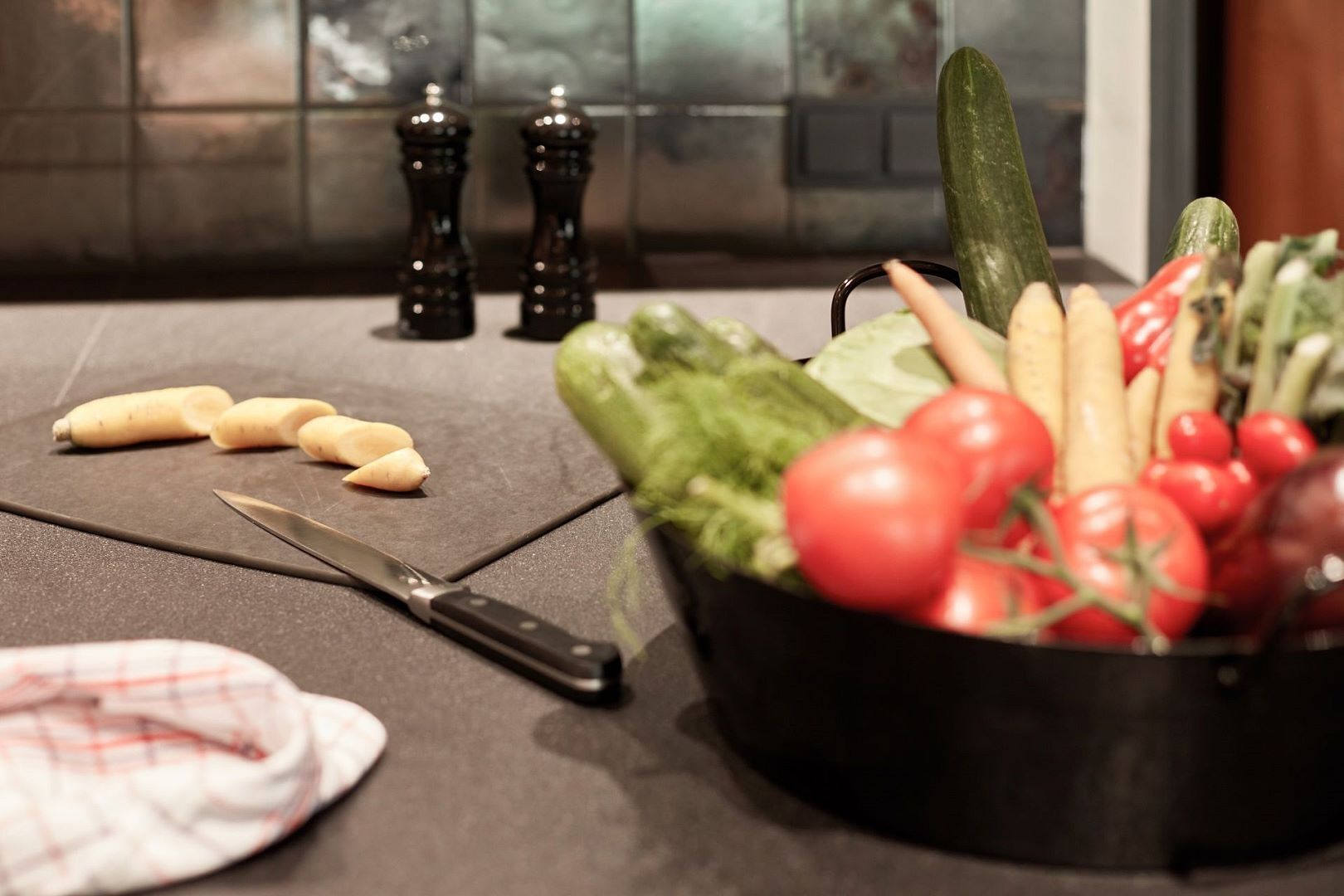 A kitchen counter with a cutting board, a knife, and a bowl of fresh vegetables.