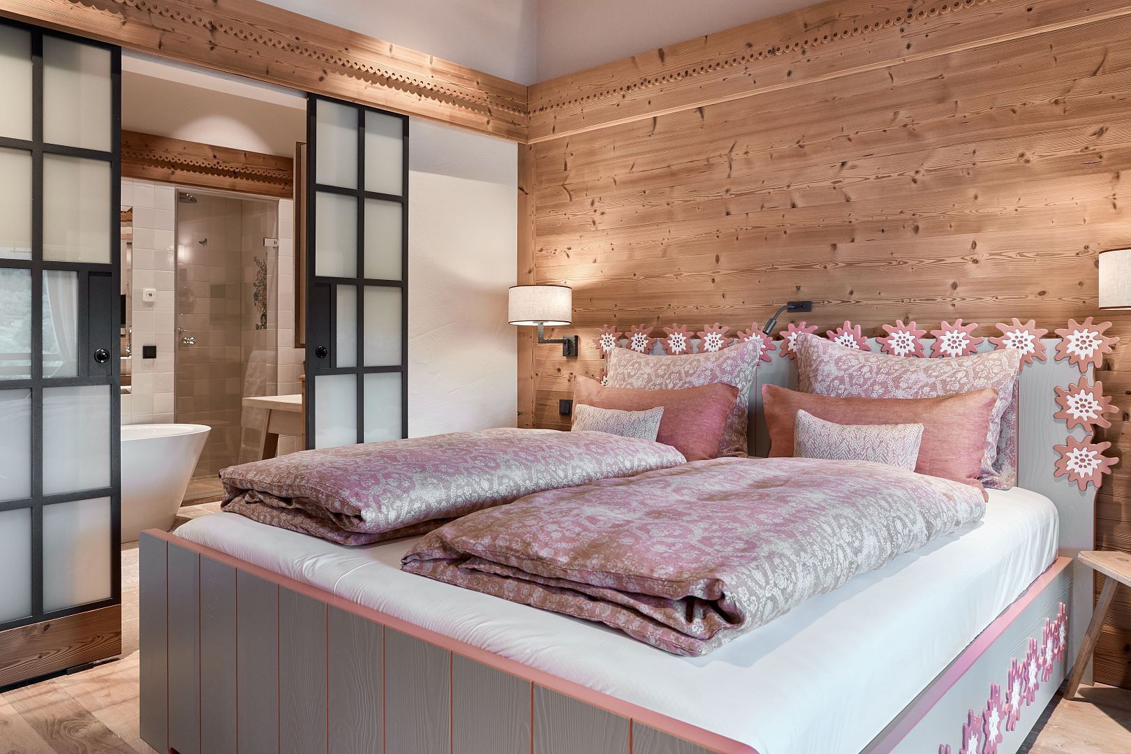 Une chambre à coucher avec une tête de lit en bois, deux lits avec une literie à motifs floraux, une table de chevet et un miroir.