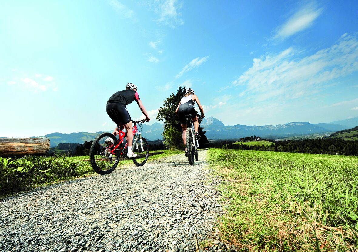 Two cyclists on a gravel path with a mountainous landscape in the background.