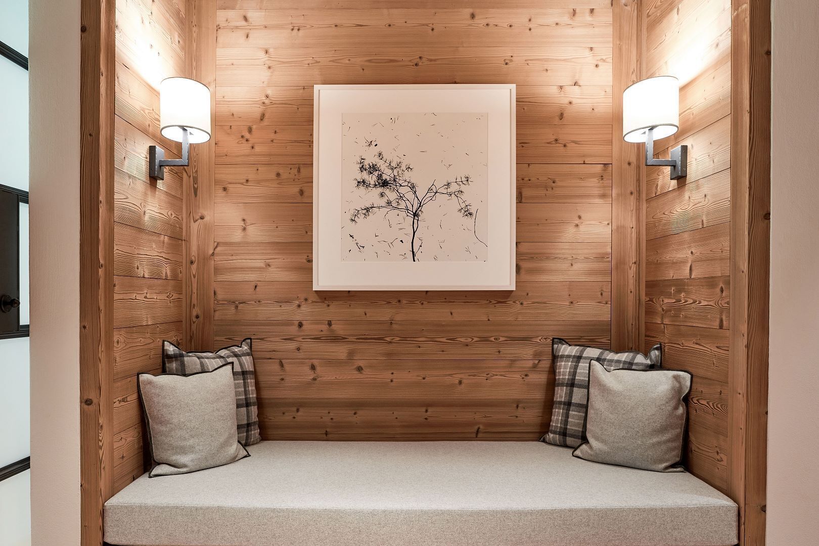 A cozy seating area with a wooden wall, two wall-mounted lights, and a framed artwork above.