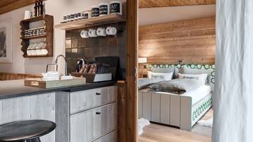 Eine moderne Küche mit Holzschränken, einer Arbeitsplatte und einem Barhocker. Ein Bett mit Holz Kopfteil und einem Zierkissen sind ebenfalls vorhanden.