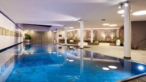 A modern indoor swimming pool with a clear blue water surface, surrounded by lounge areas with seating and potted plants. - Kitzbühel Lodge (Reith bei Kitzbuehel)