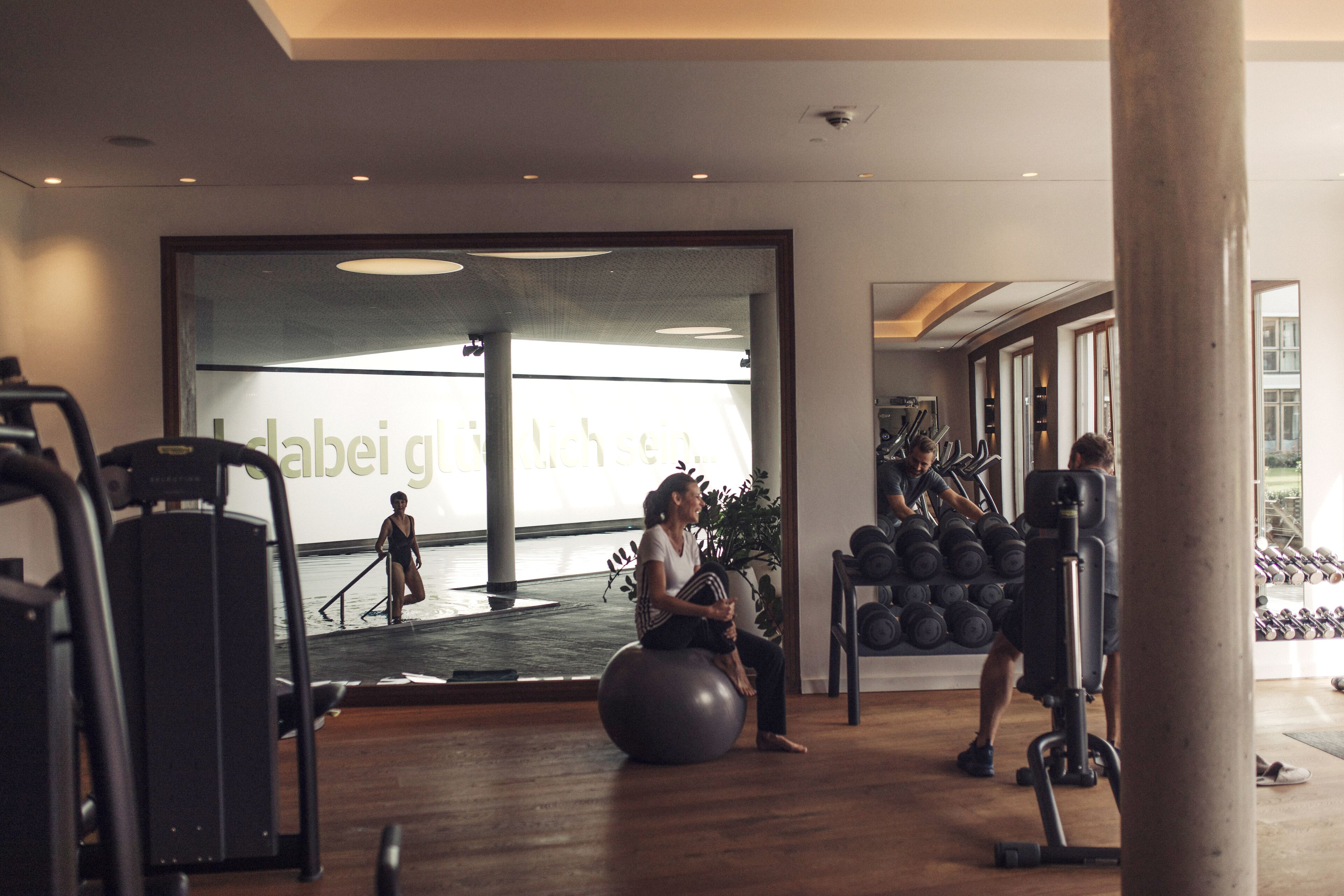 Un gimnasio con equipo de ejercicio, una mujer sentada y un hombre entrenando.