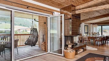Ein geräumiger Wohnbereich mit Holzbalkendecke, einem Hängekorbstuhl, einem Kamin und einem Essbereich mit Tisch und Stühlen.