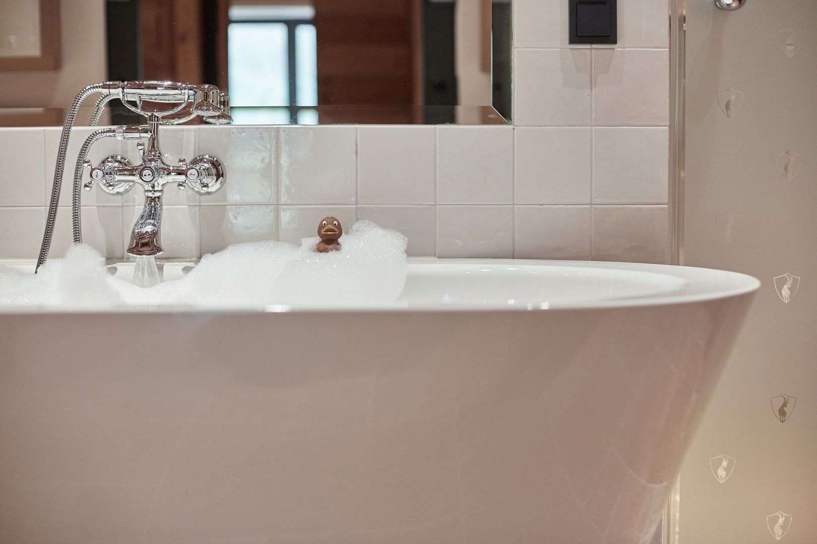 Een bad vol bruisende bubbels, een chromen kraan en een witte betegelde muur.