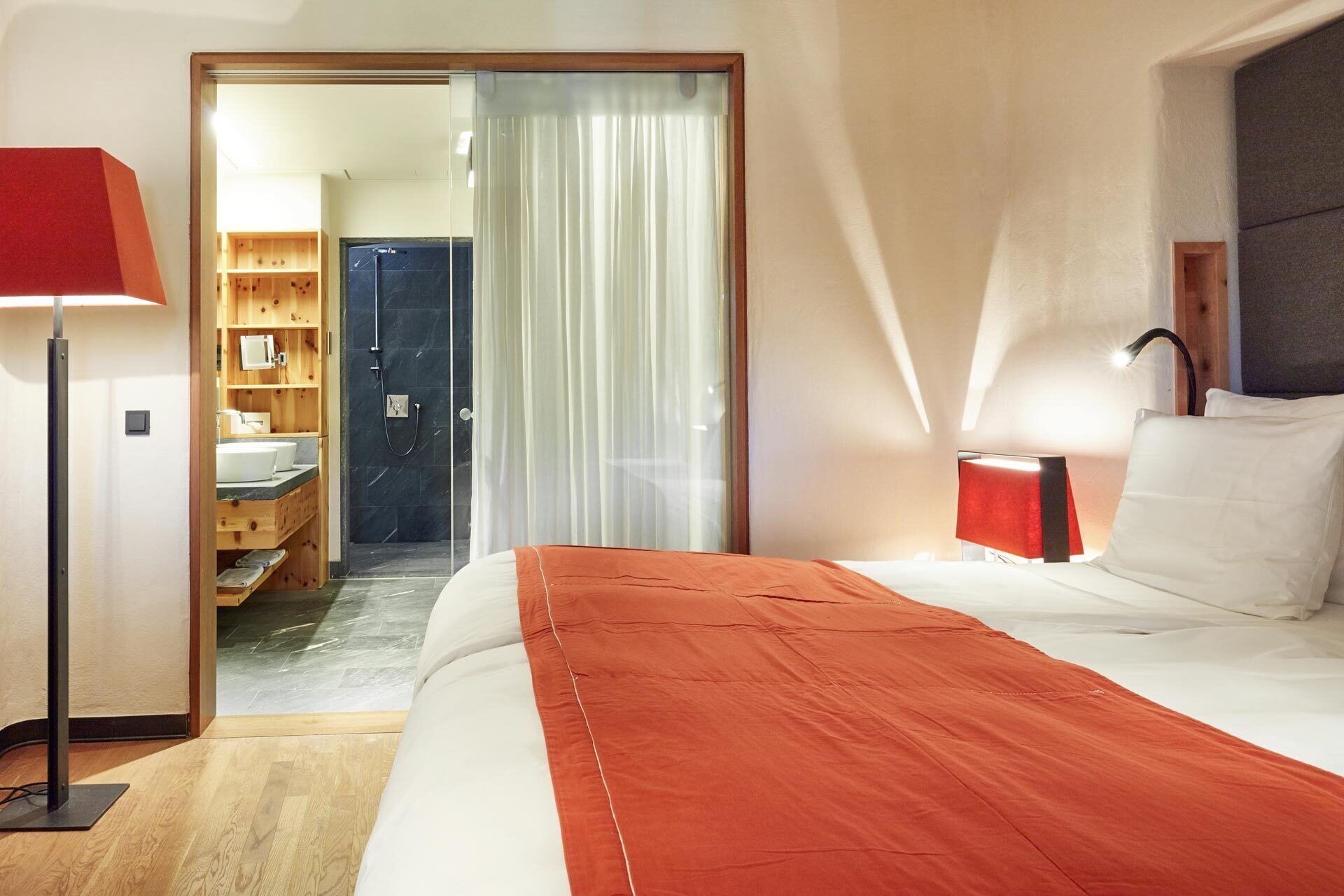 Ein Hotelzimmer mit einem Bett, einem Nachttisch, einer Lampe, einem Holzschrank und einem durch eine offene Tür einsehbaren Badezimmer.