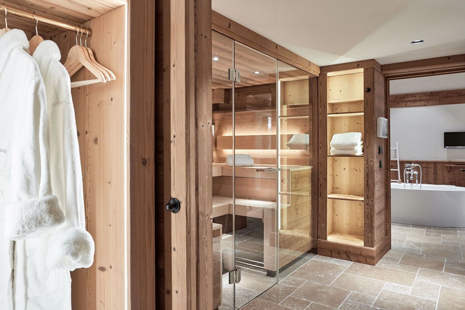 Ein begehbarer Kleiderschrank aus Holz mit Glastüren, einem eingebauten Regal und einem Badezimmer mit Badewanne und Spiegel.