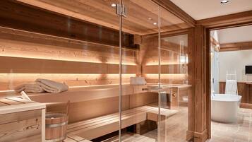 A modern spa room with wooden paneling, a glass-enclosed sauna, a wooden bench, and a stone-tiled floor.