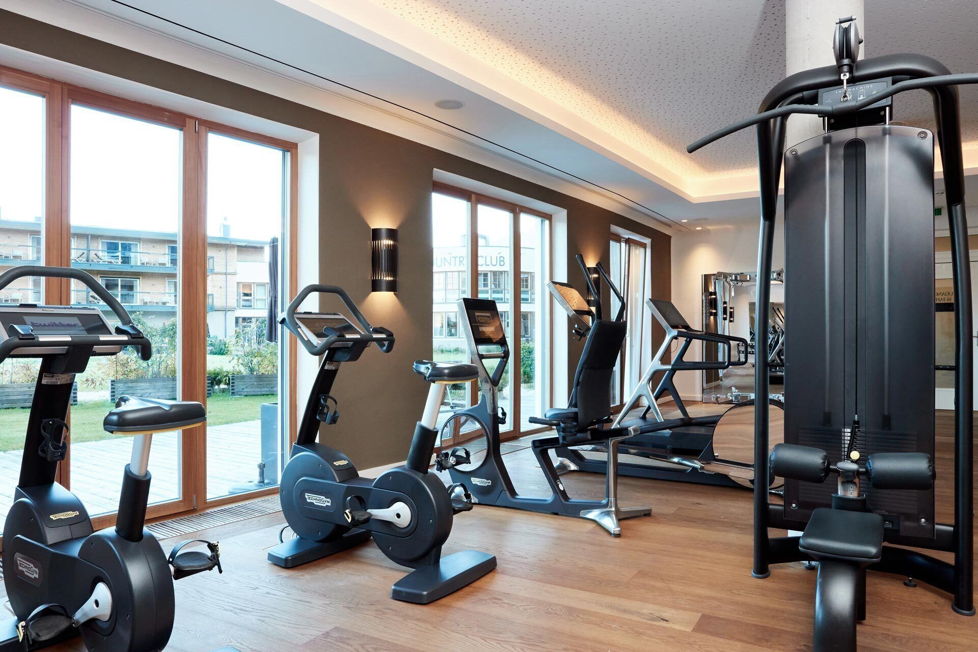 Une salle de sport moderne équipée de divers appareils d’exercice, dotée de grandes fenêtres et offrant une vue sur l’extérieur.