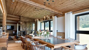 A modern dining area with a wooden table and chairs, a fireplace, and large windows offering a view of the outdoors. - Kitzbühel Lodge (Reith bei Kitzbuehel)
