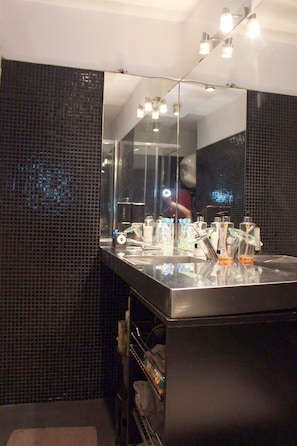 A modern bathroom with a large mirror, black tiled walls, and a glass countertop with toiletries.