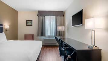 Habitación de hotel con cama, escritorio, silla, televisor, lámpara, equipo de aire acondicionado y un cartel de bienvenida enmarcado.