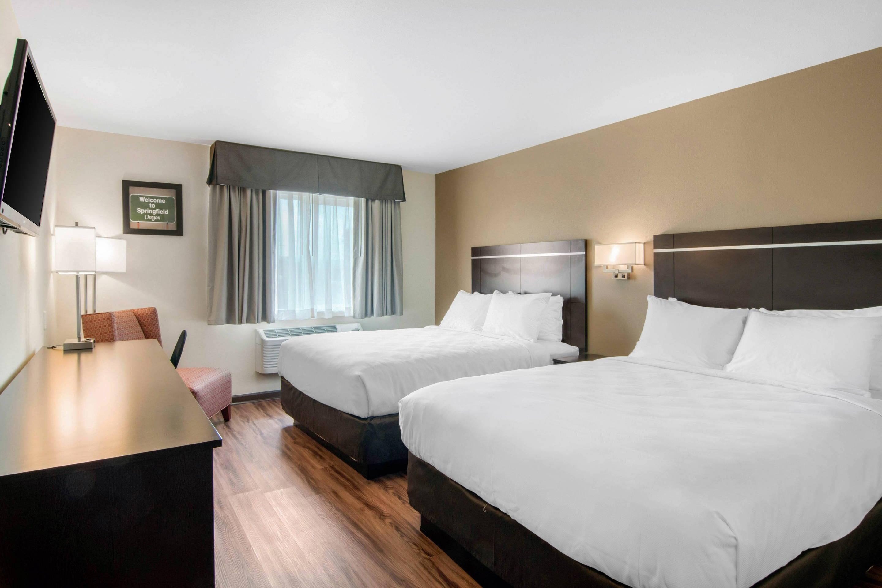 A hotel room with two beds, a desk, a TV, and a window with curtains.