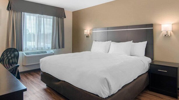 A hotel room with a large bed, a desk, and a chair. There is a window with curtains, a wall-mounted air conditioner, and two wall sconces. - Econo Lodge Inn & Suites Springfield Main Street (Springfield)