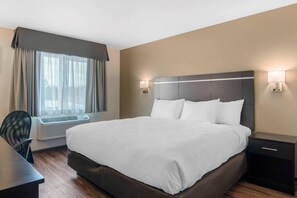 Habitación de hotel con una cama grande, un escritorio y una silla. Hay una ventana con cortinas, un aire acondicionado instalado en la pared y dos apliques.
