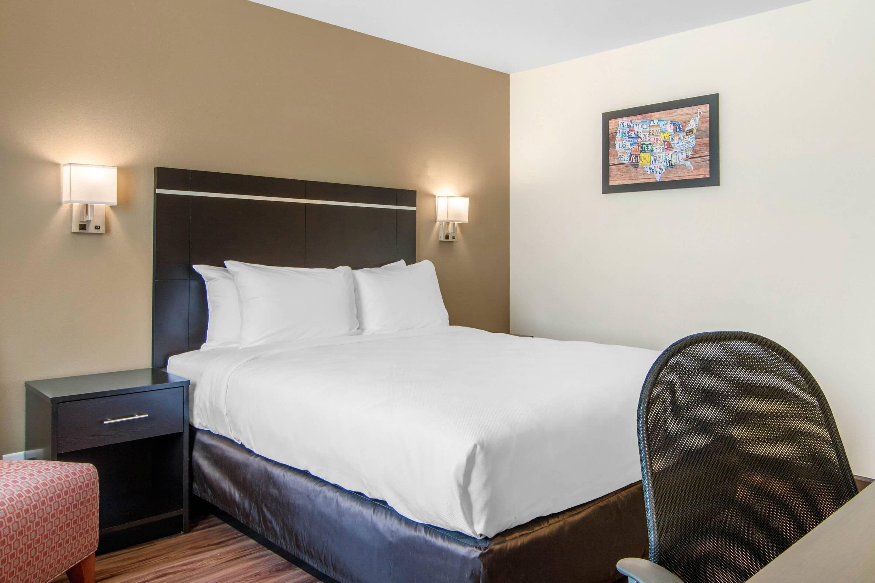 A hotel room with a bed, bedside tables, a chair, and a wall-mounted map.