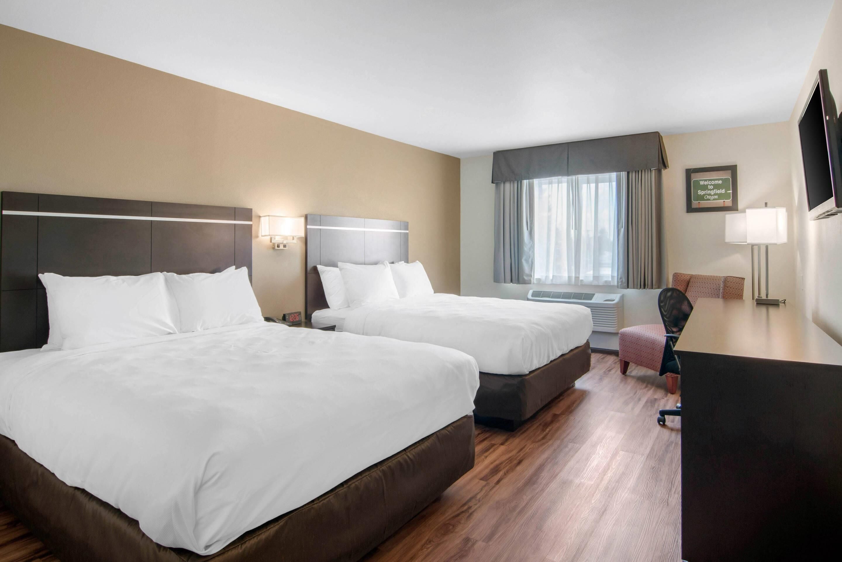 A hotel room with two beds, a desk, a chair, a TV, and a window with curtains.